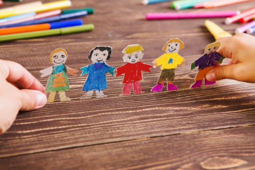 iStock-854125684-500x333 the child does figures of people of paper. Paper people on wooden background. Creative child play with craft.