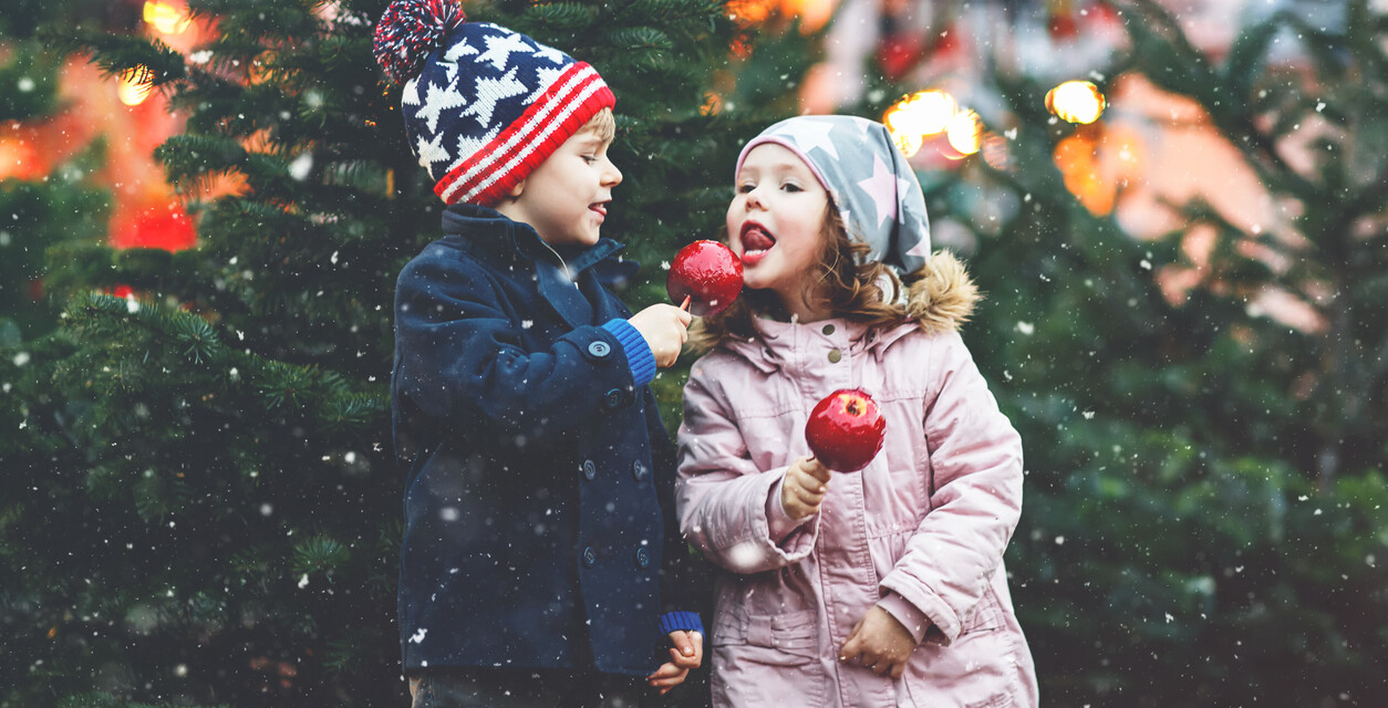 Kinder mit kandiertem Apfel vor Tannenbäumen